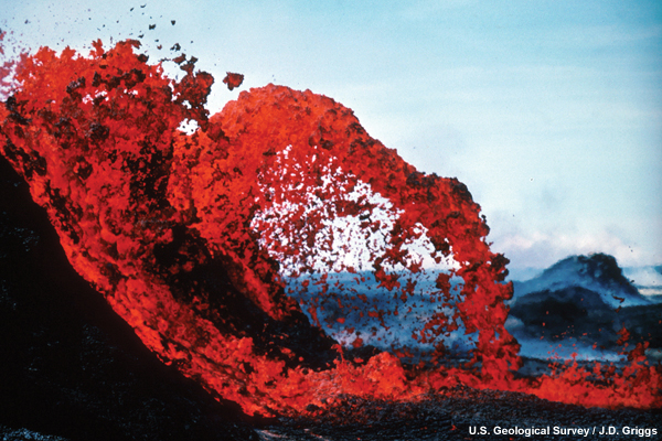 Eruption of Kilauea Volcano beginning in 1983. Arching lava fountain - bright red lava is arching from the side of a slope and to the right.